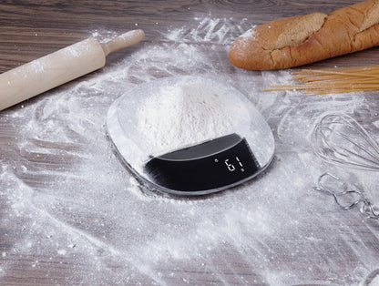 Digital kitchen scale on a flour-dusted surface with bread and pasta in the background